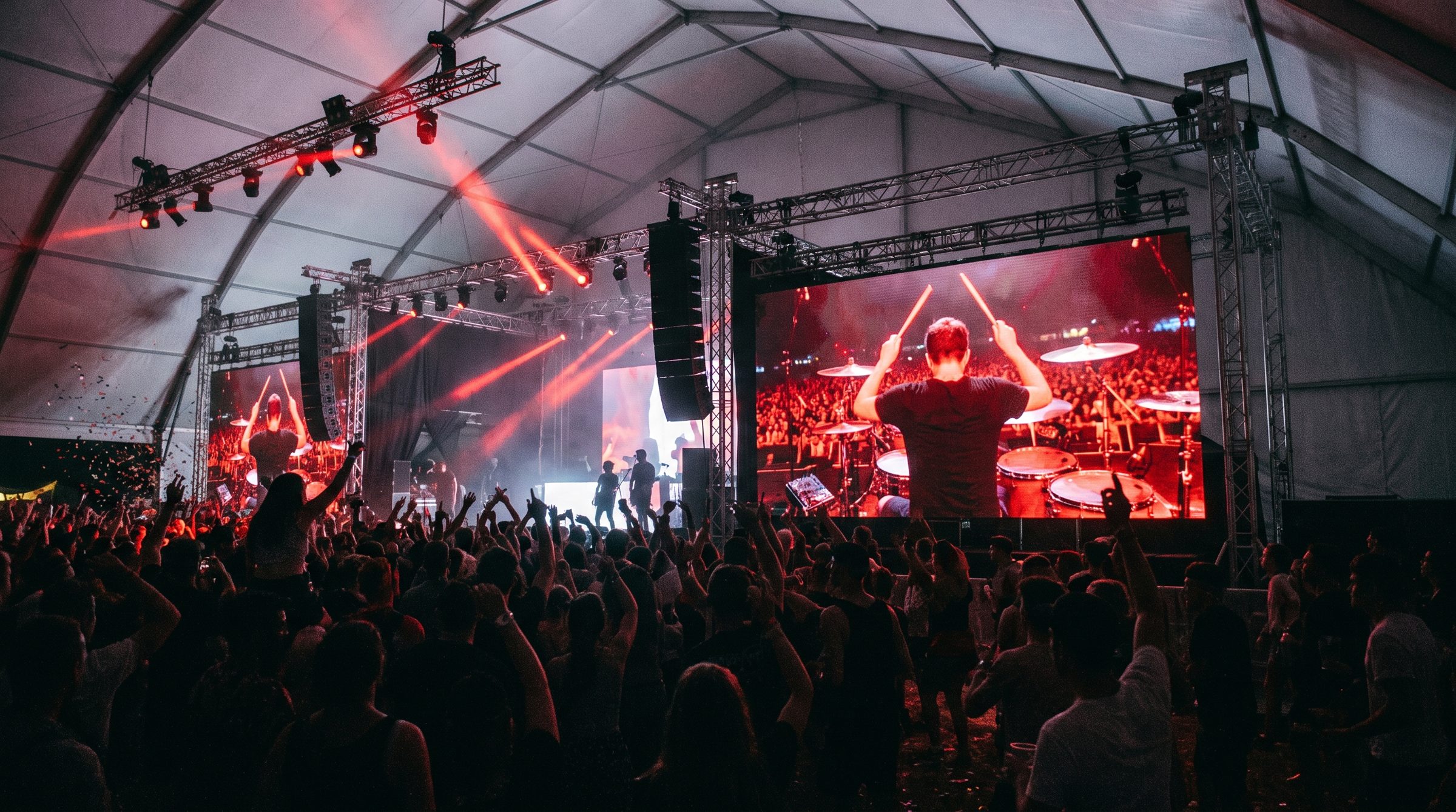 Festivaltent vol publiek voor een LED-scherm met de drummer live in beeld